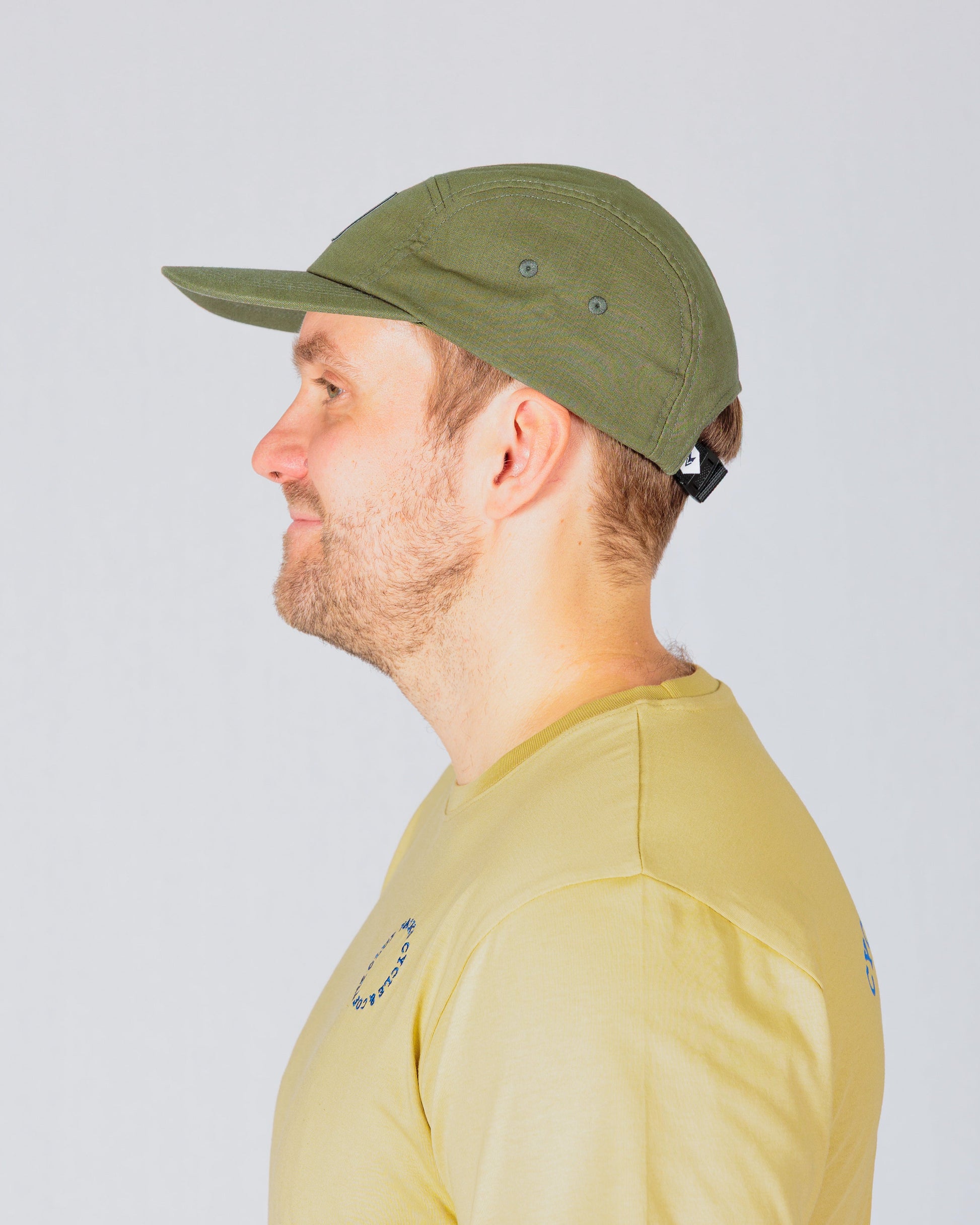 Man in a light yellow t-shirt and green cap facing left against a plain light background.