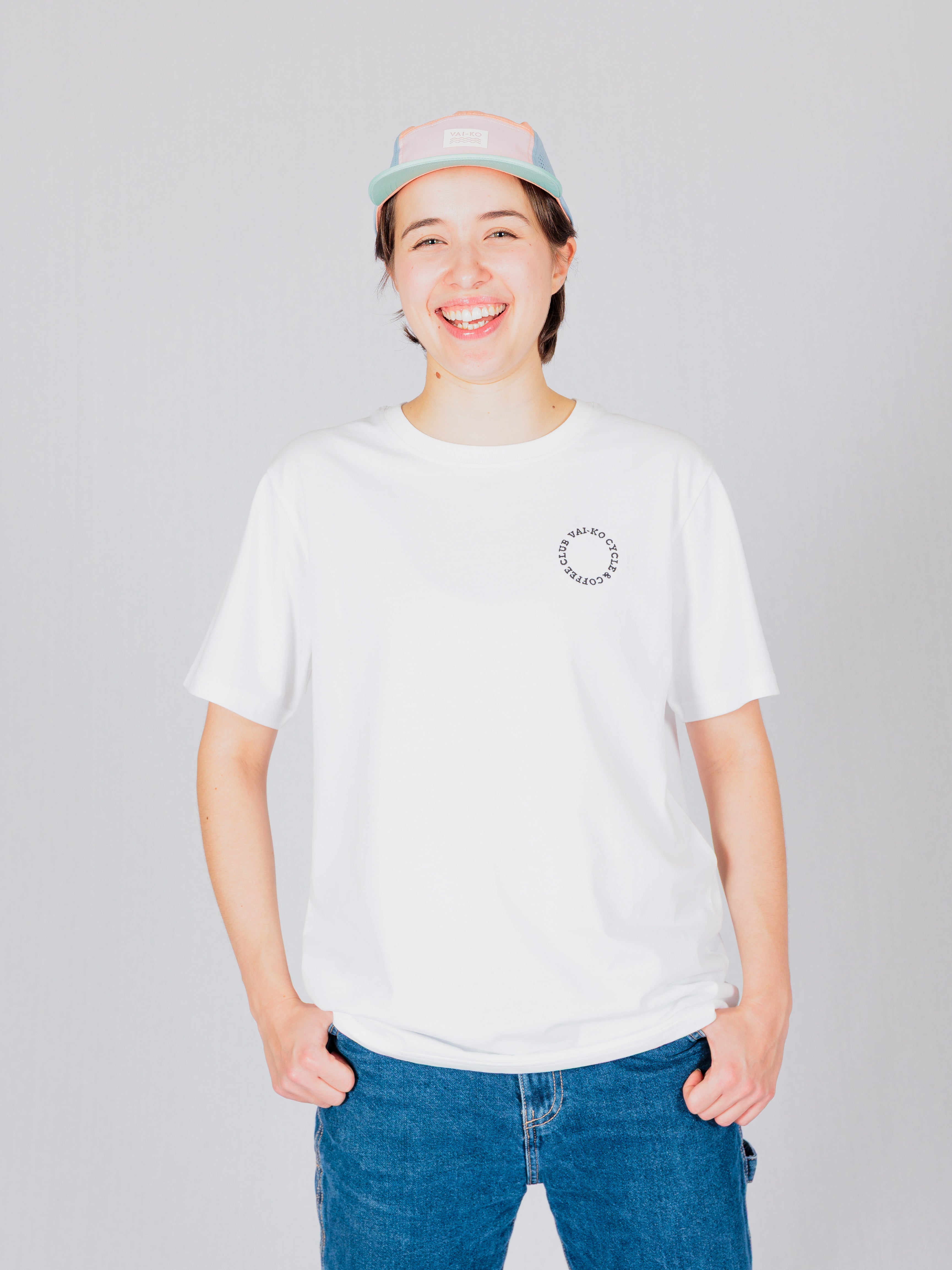 Person in a white t-shirt and pastel cap smiling, standing against a light gray background.