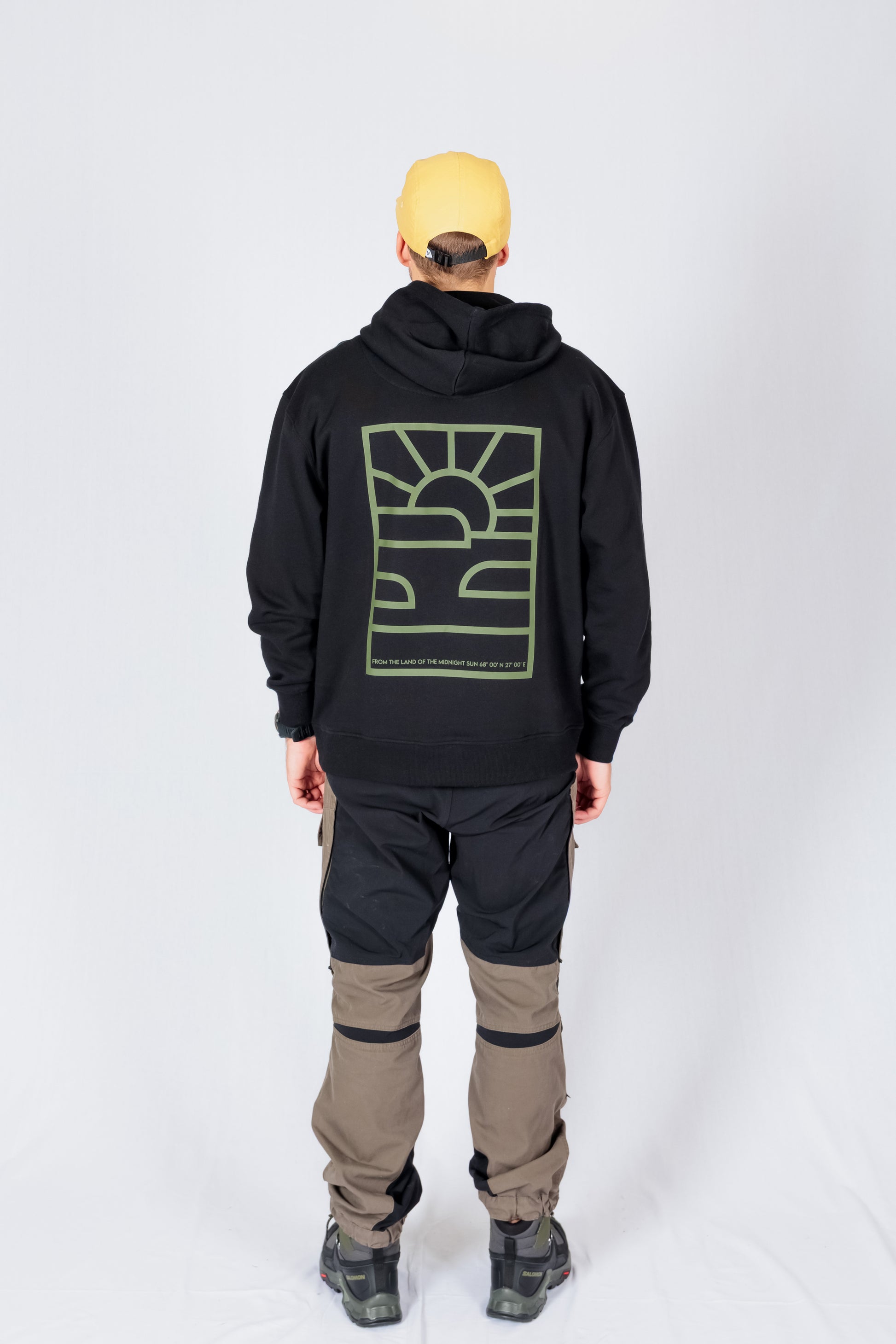 Person wearing a yellow cap, black hoodie with a green graphic, and two-tone cargo pants, seen from behind.