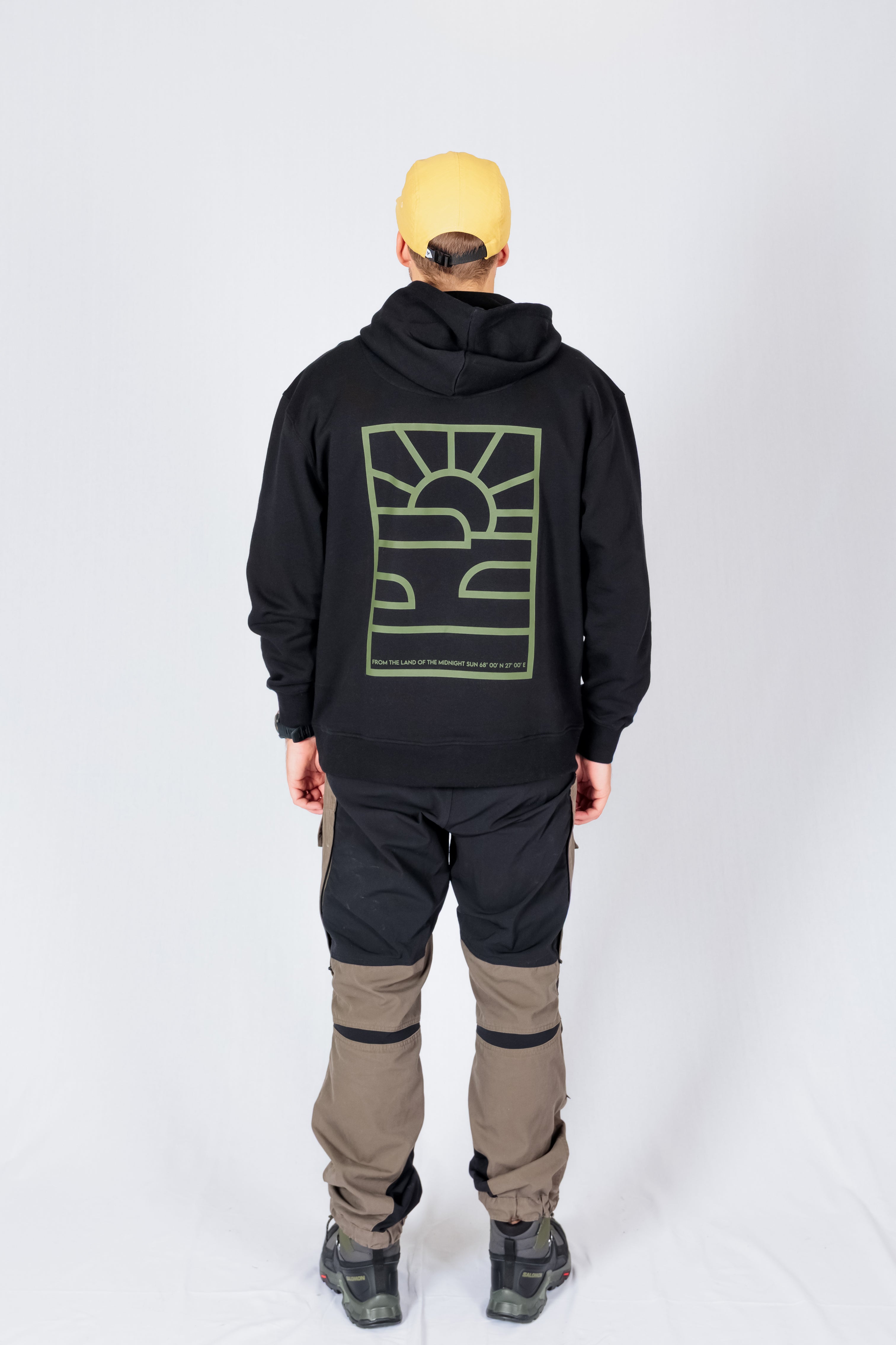 Person wearing a yellow cap, black hoodie with a green graphic, and two-tone cargo pants, seen from behind.