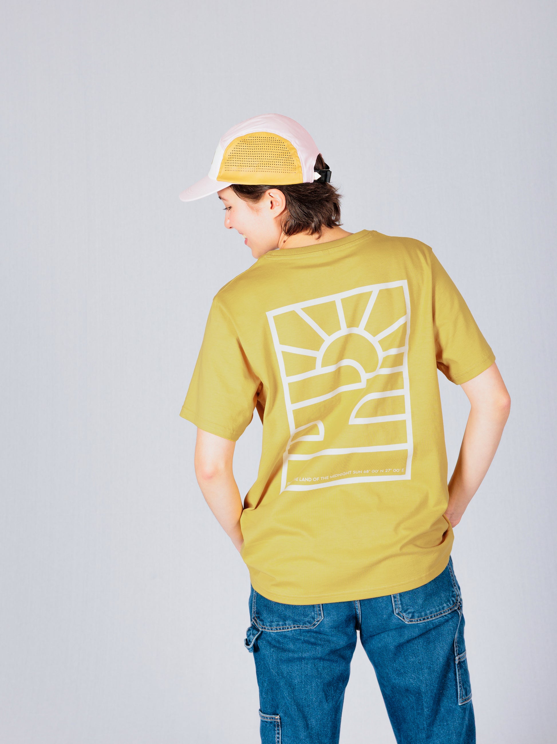 Person in yellow t-shirt with sun graphic and jeans, wearing a pink cap, facing away from the camera.