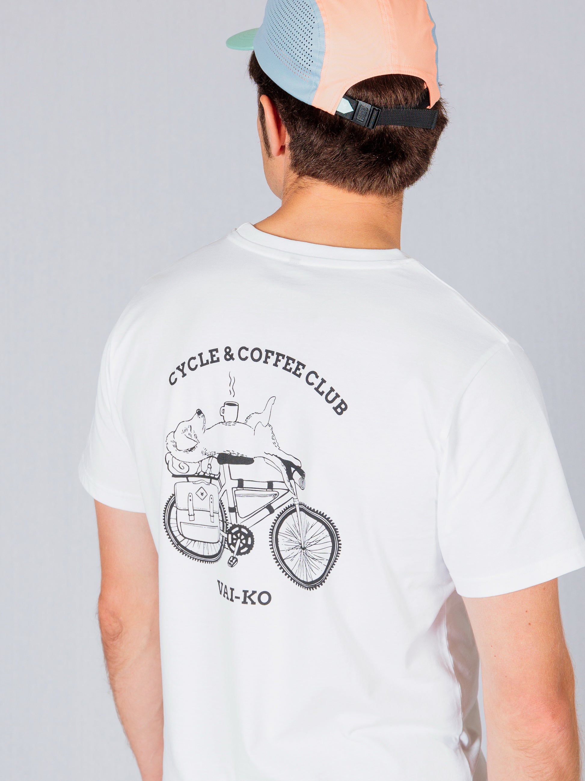 Man in a white T-shirt and pastel cap, with Cycle & Coffee Club graphic and a bike illustration on the back.