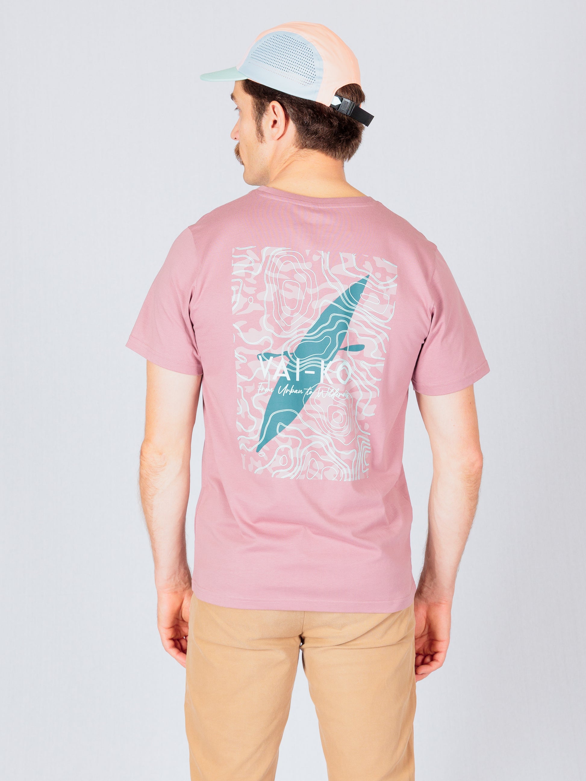 Man wearing a pink graphic T-shirt and beige pants, facing away, with a cap on his head.