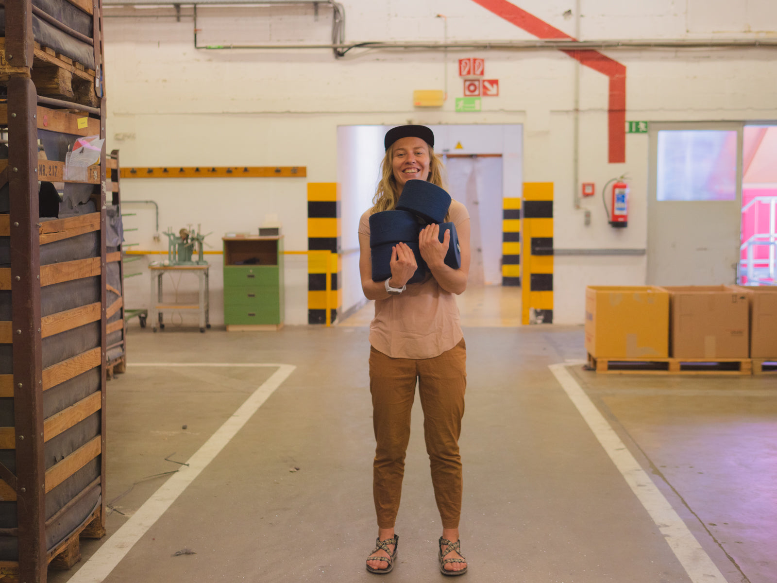 Person smiling and holding a rolled mat, standing in a spacious warehouse with boxes and shelves.