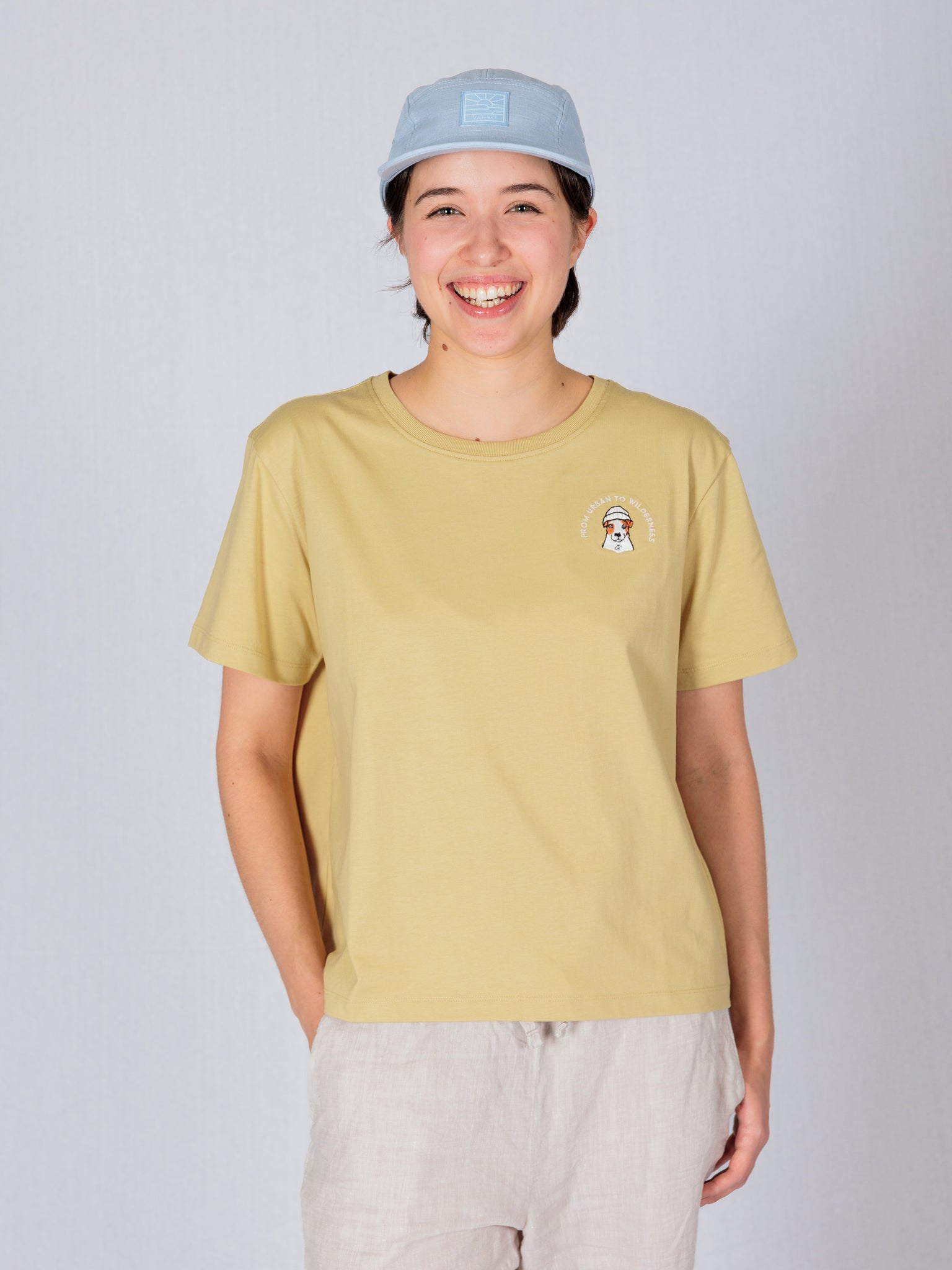 Smiling person wearing a yellow t-shirt and light blue cap, standing against a plain light background.