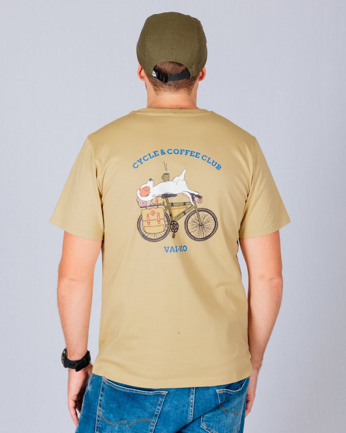 Man in a tan cap and t-shirt with a graphic of a cat on a bike, standing against a plain background.