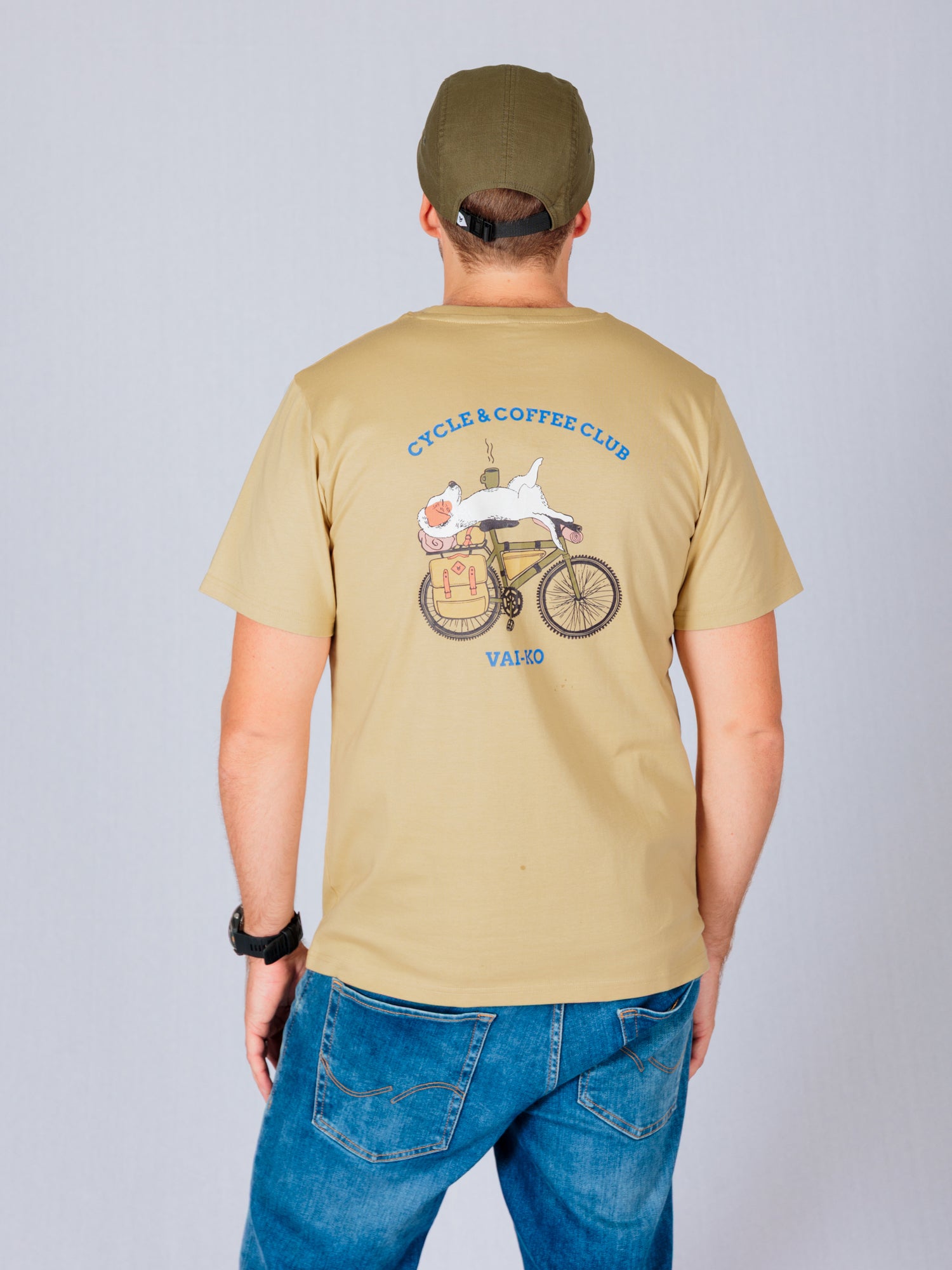 Man in a tan cap and t-shirt with a graphic of a cat on a bike, standing against a plain background.