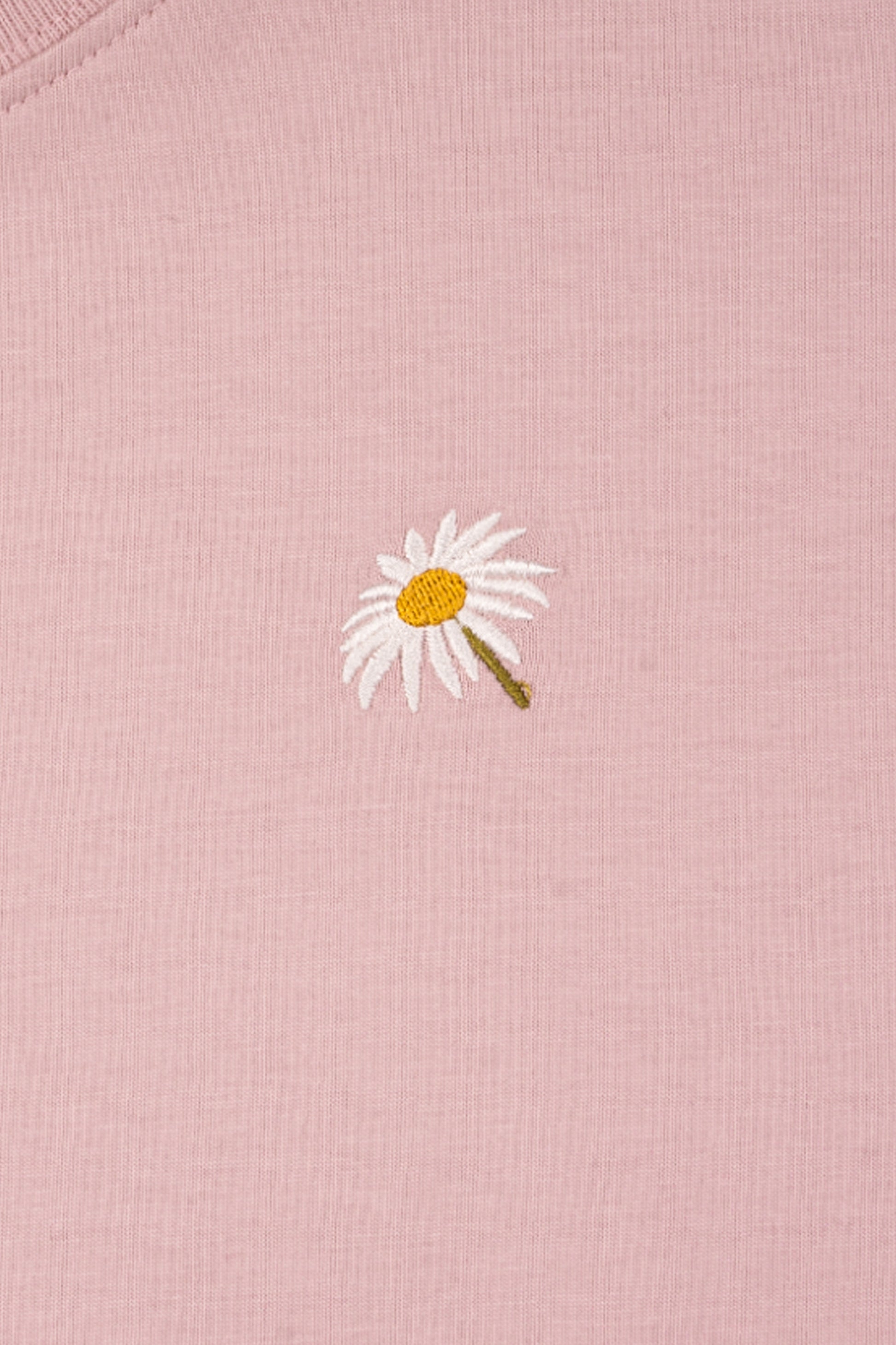 A small embroidered white daisy with a yellow center on a light pink fabric background.