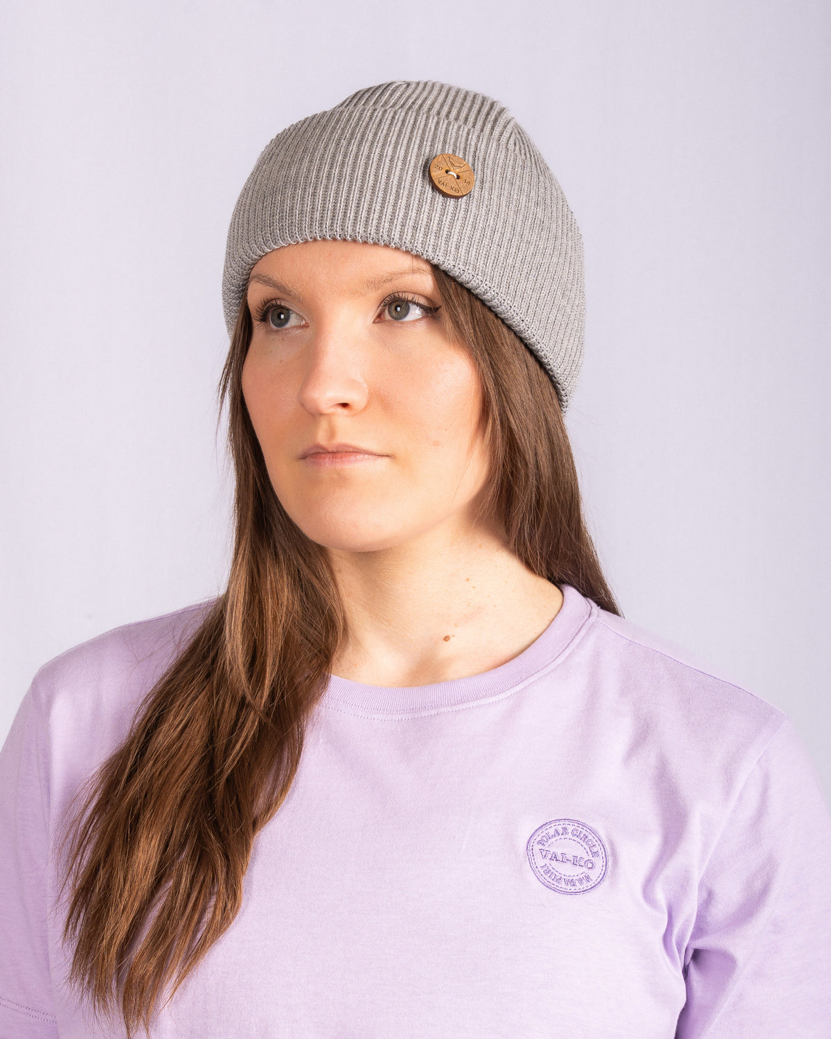 Woman in a gray knit beanie and lavender shirt, looking slightly to the left, against a plain background.