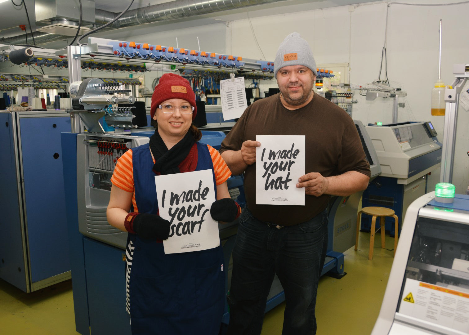 Two people in a knitting factory hold signs reading I made your scarf and I made your hat.