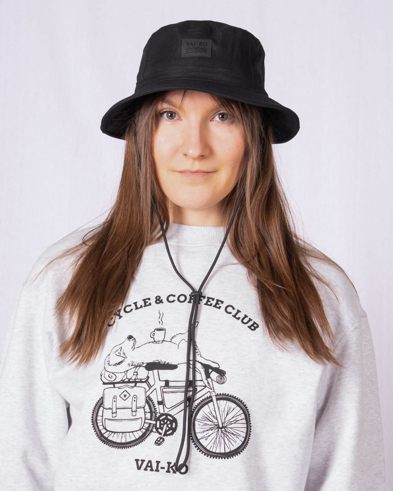 Woman in a black bucket hat and gray sweatshirt with a bicycle graphic, posing against a plain background.