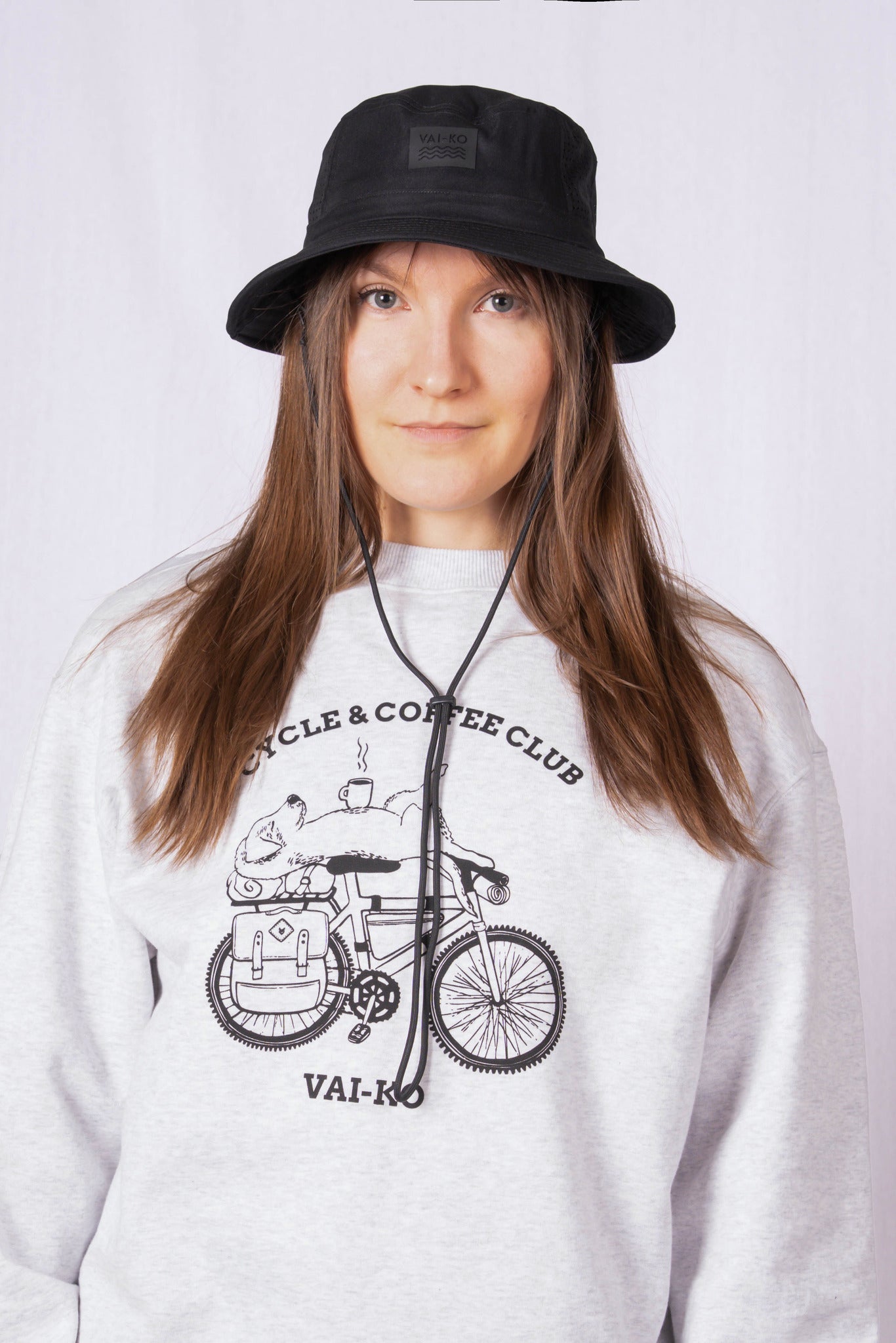 Woman in a black bucket hat and gray sweatshirt with a bicycle graphic, posing against a plain background.