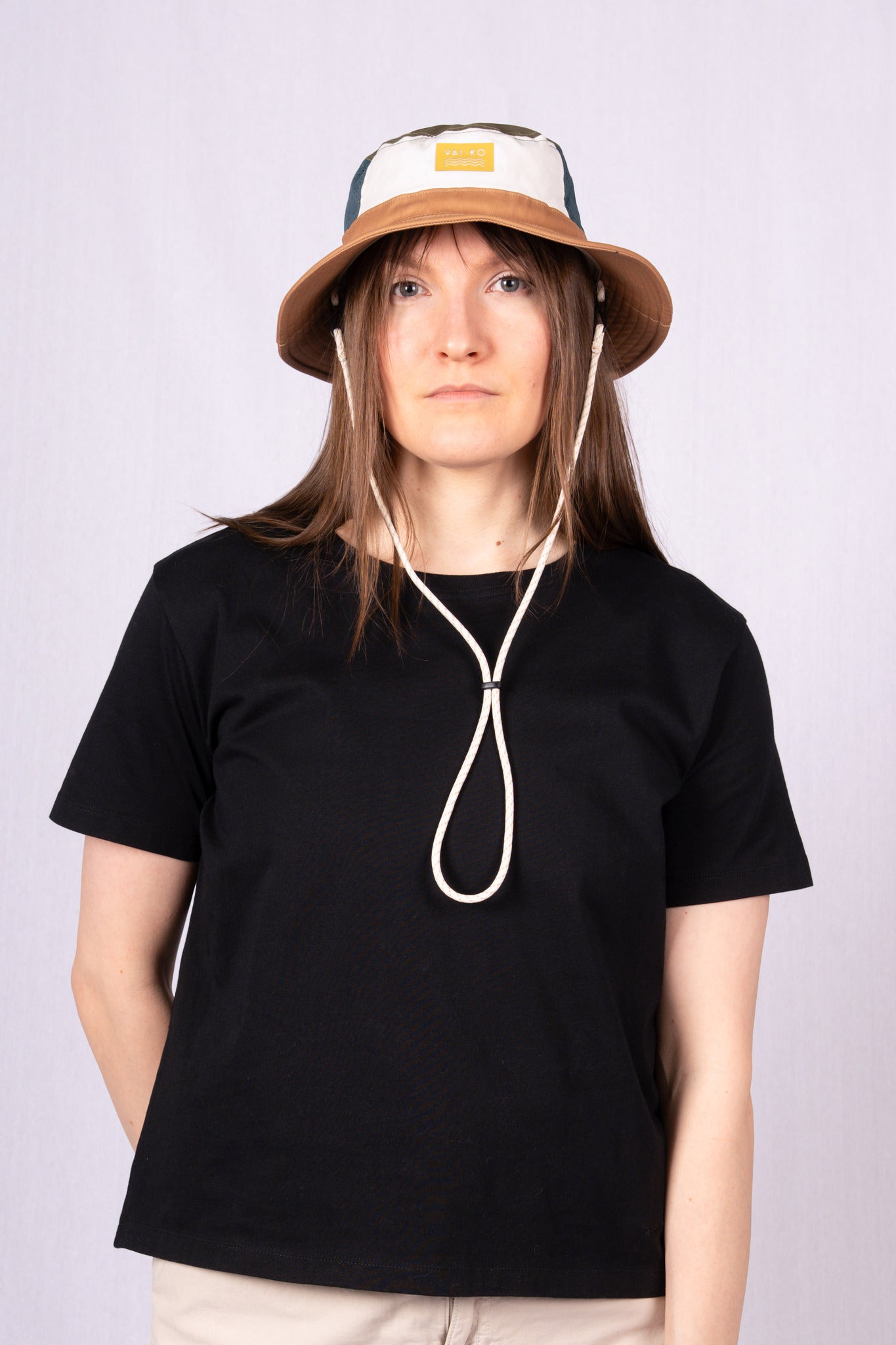 Person wearing a black t-shirt and a beige bucket hat with chin straps, standing against a plain background.