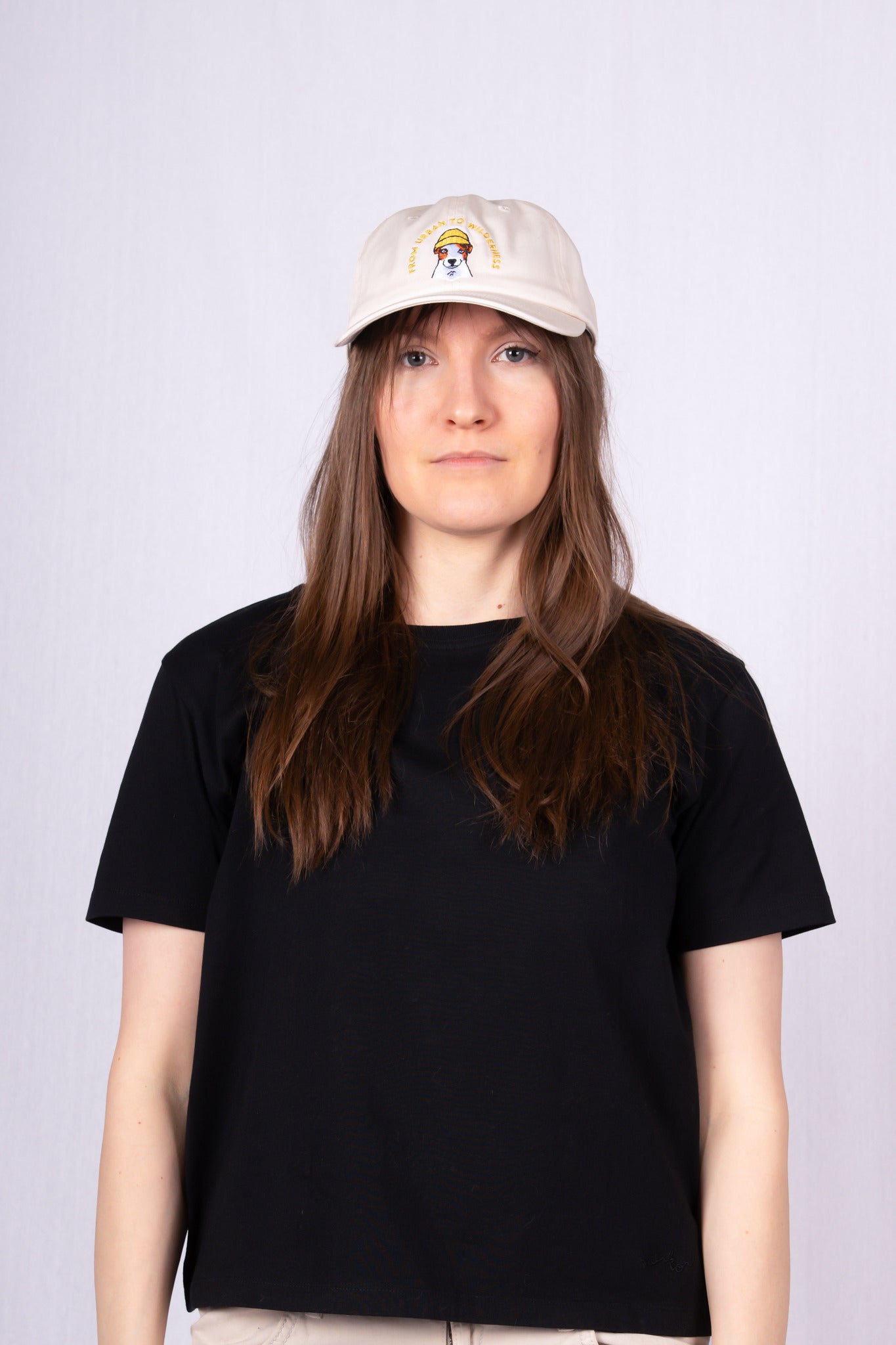 Woman in a black t-shirt and beige hat with a cartoon graphic, standing against a light background.