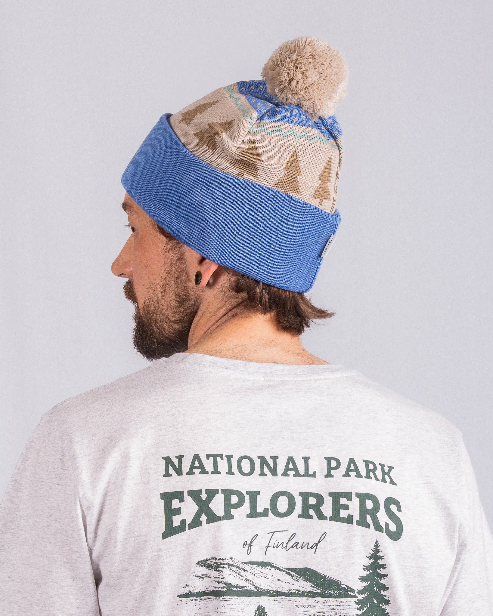 Man in a blue and tan beanie with pompom, wearing a National Park Explorers t-shirt, facing away.