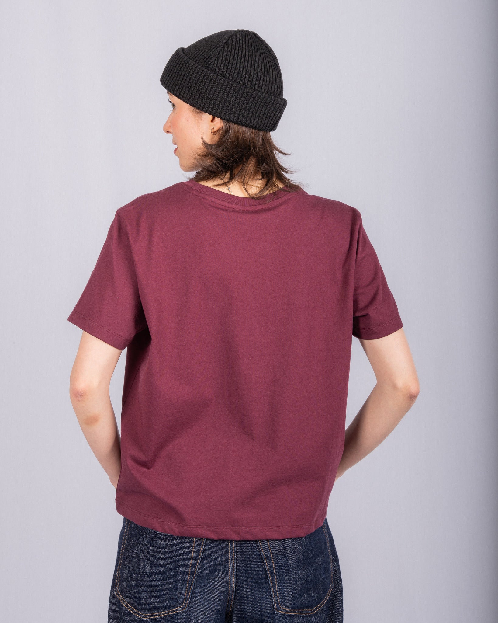 Person in a maroon t-shirt, black beanie, and jeans standing with their back to the camera.