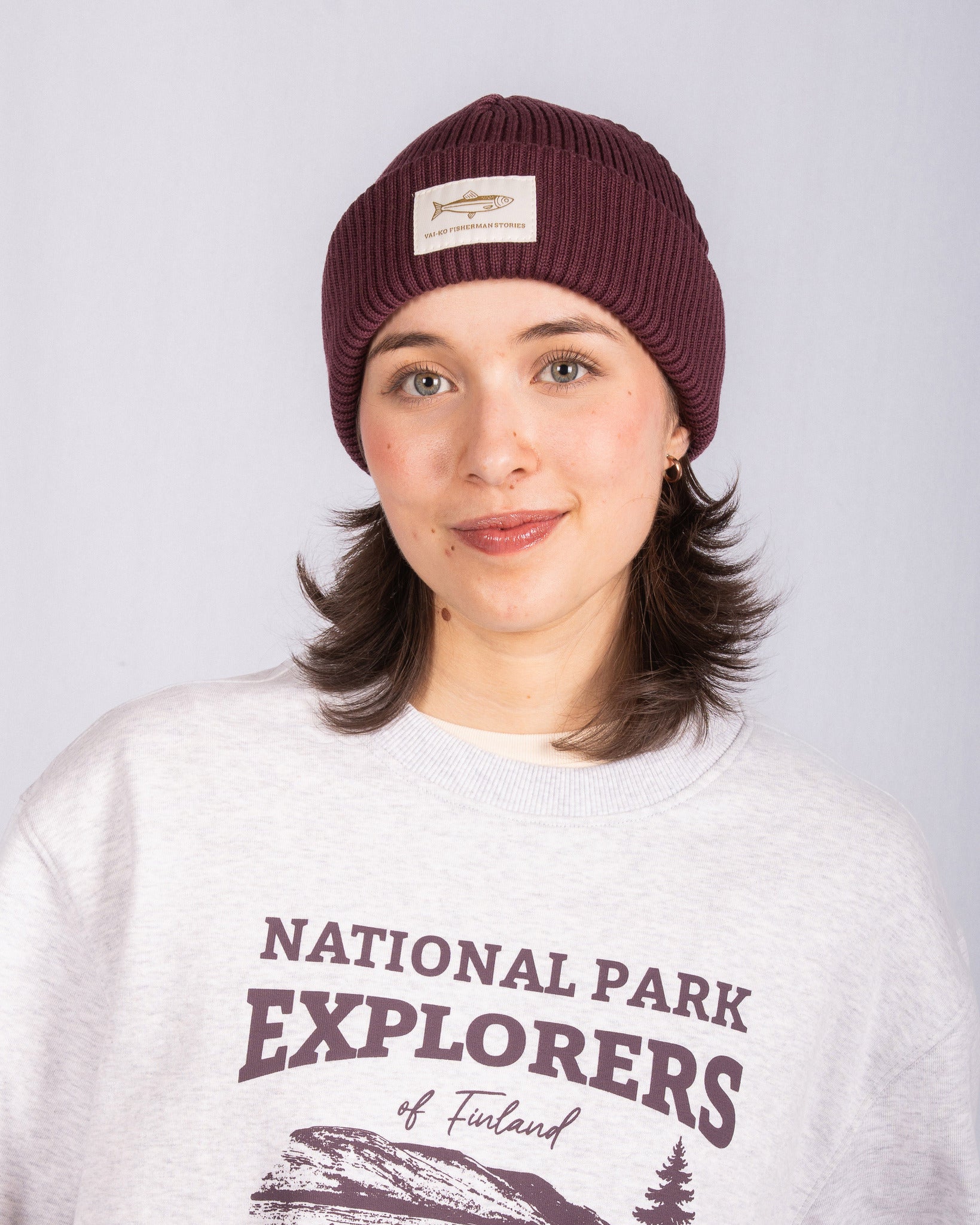 Woman in a maroon beanie and National Park Explorers of Finland sweatshirt, smiling at camera.