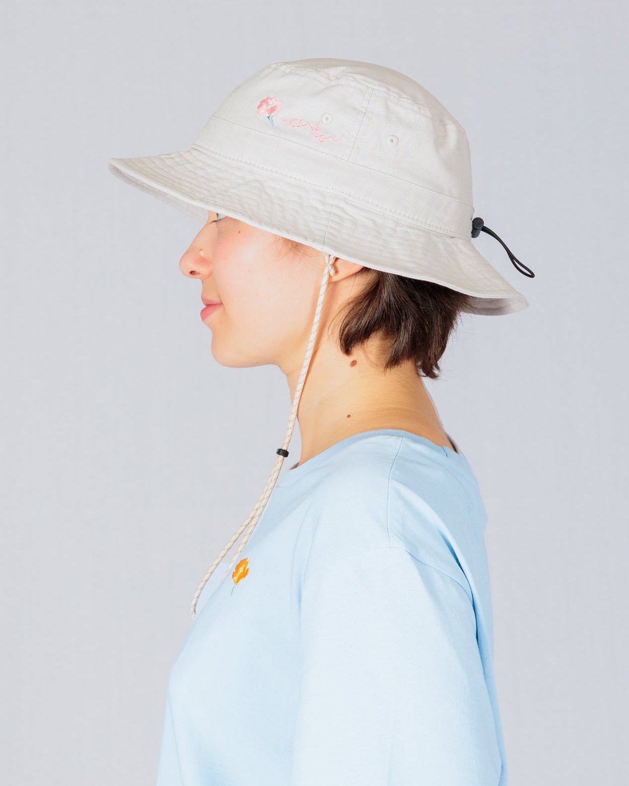 Person in a light blue shirt and beige bucket hat, shown in profile against a plain light background.
