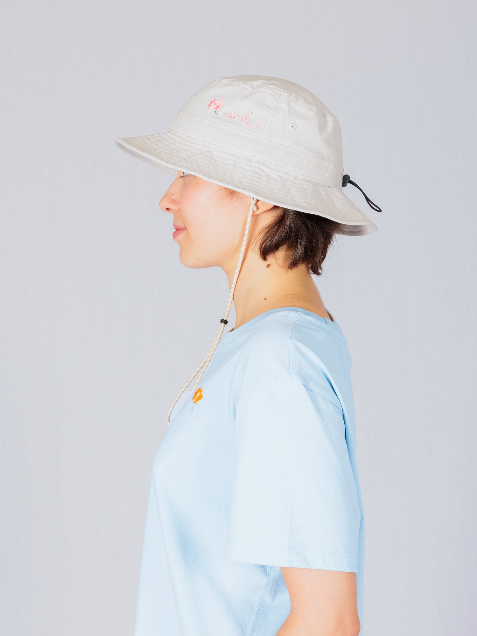 Person in a light blue shirt and beige bucket hat, shown in profile against a plain light background.