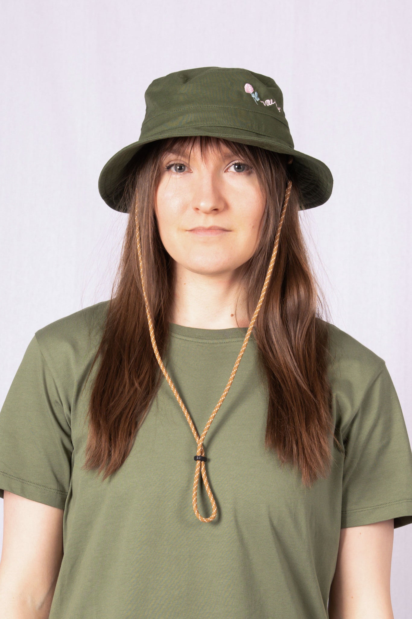 Woman in an olive green bucket hat and matching shirt, looking at the camera with a neutral expression.