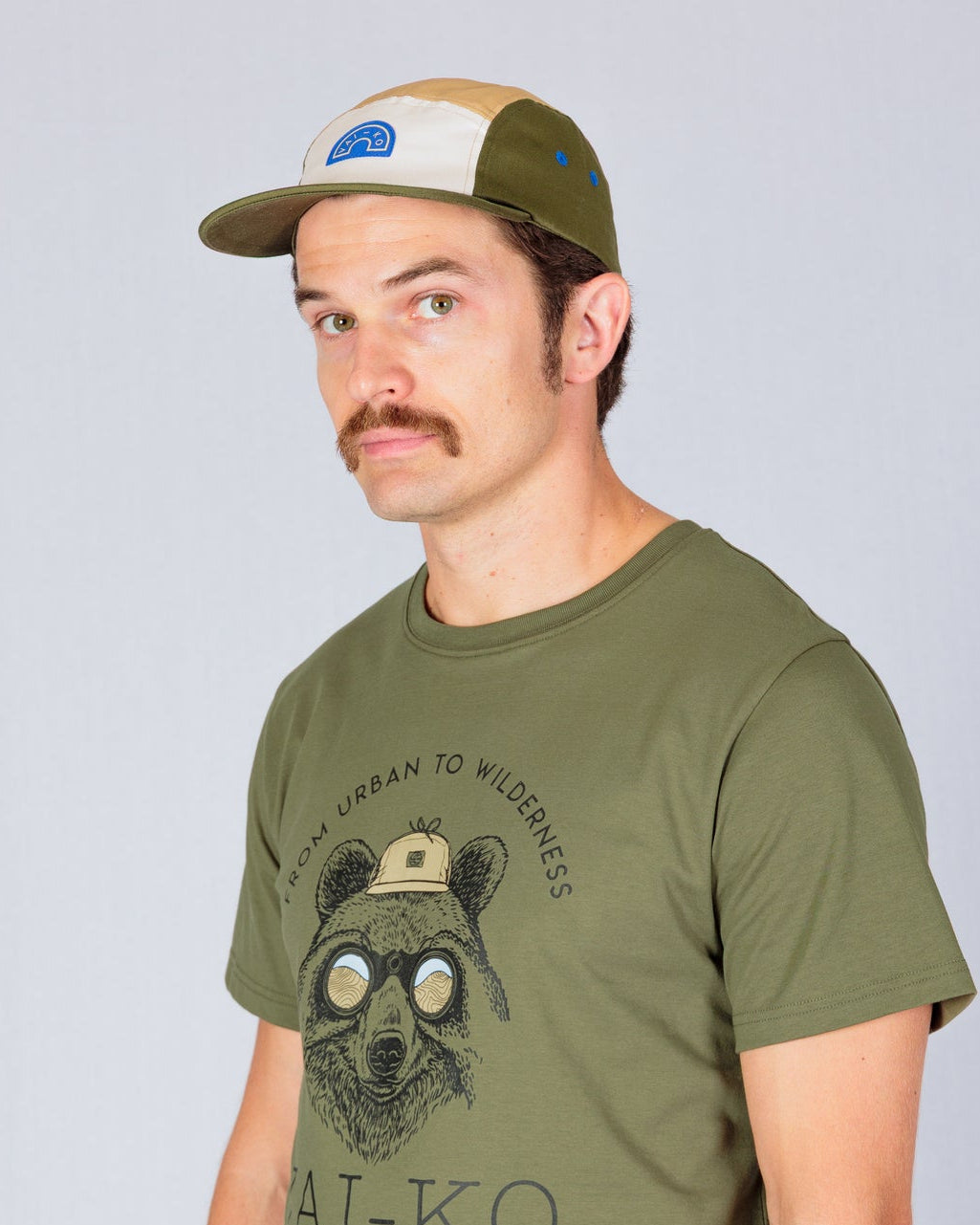 Man in a green graphic t-shirt and cap standing against a plain light background, looking at the camera.
