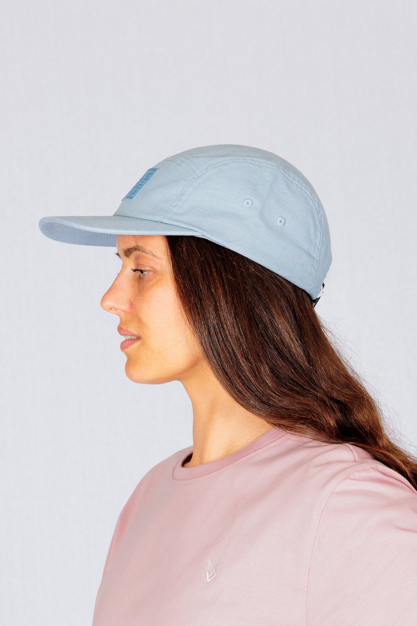 Woman in a light blue cap and pink shirt, shown in profile against a plain light background.