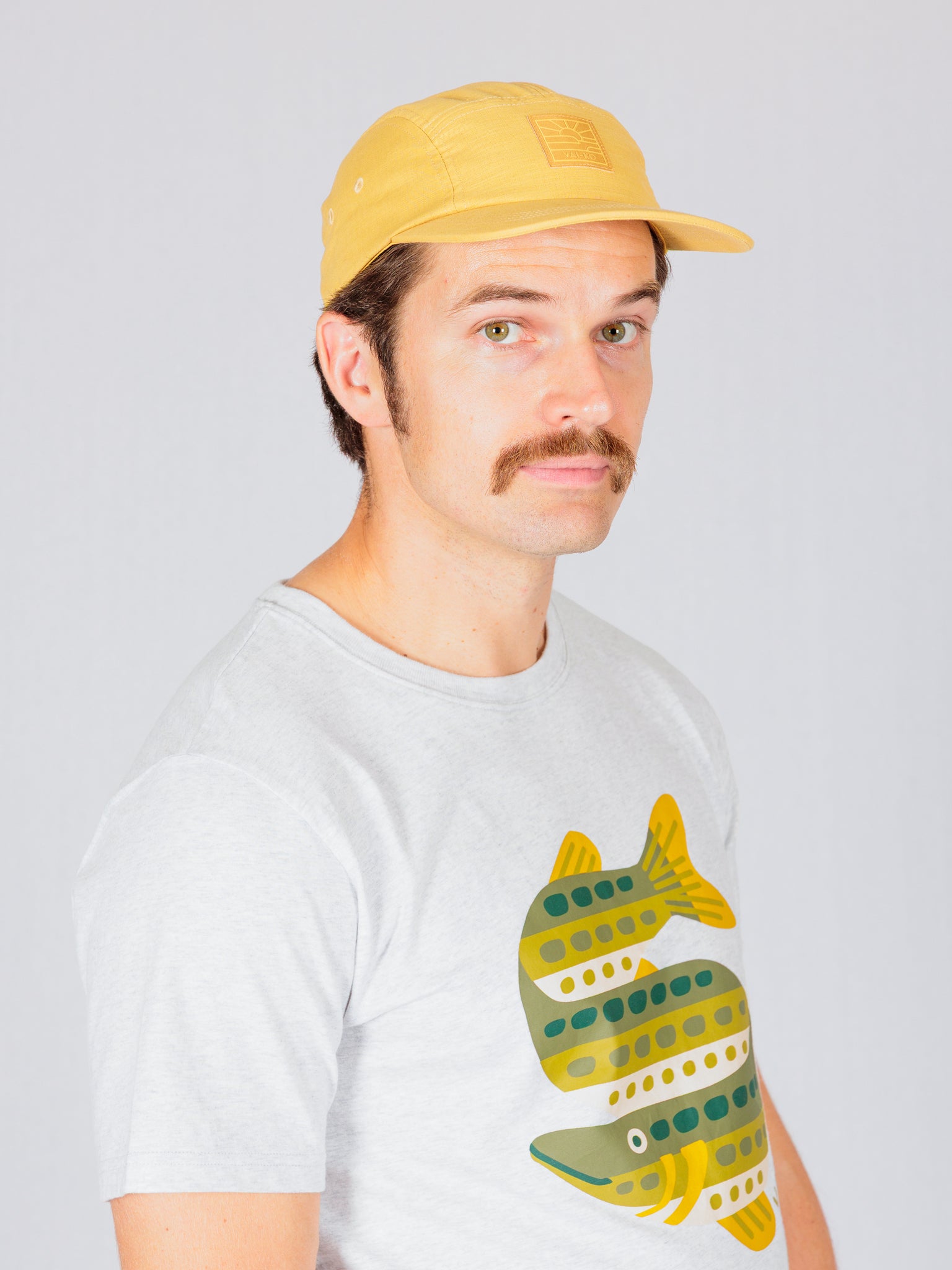 Man in a yellow cap and gray shirt with a green fish graphic, looking at the camera.