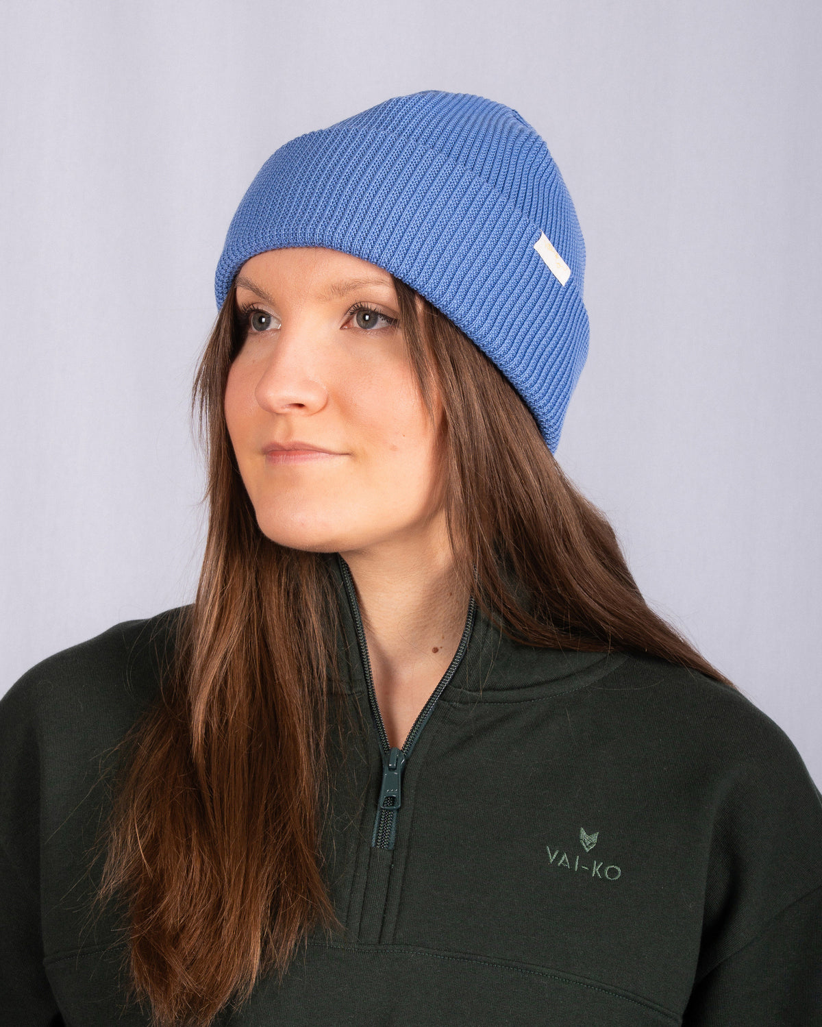 Woman wearing a blue knit beanie and dark green zip-up sweater, facing slightly to the left.