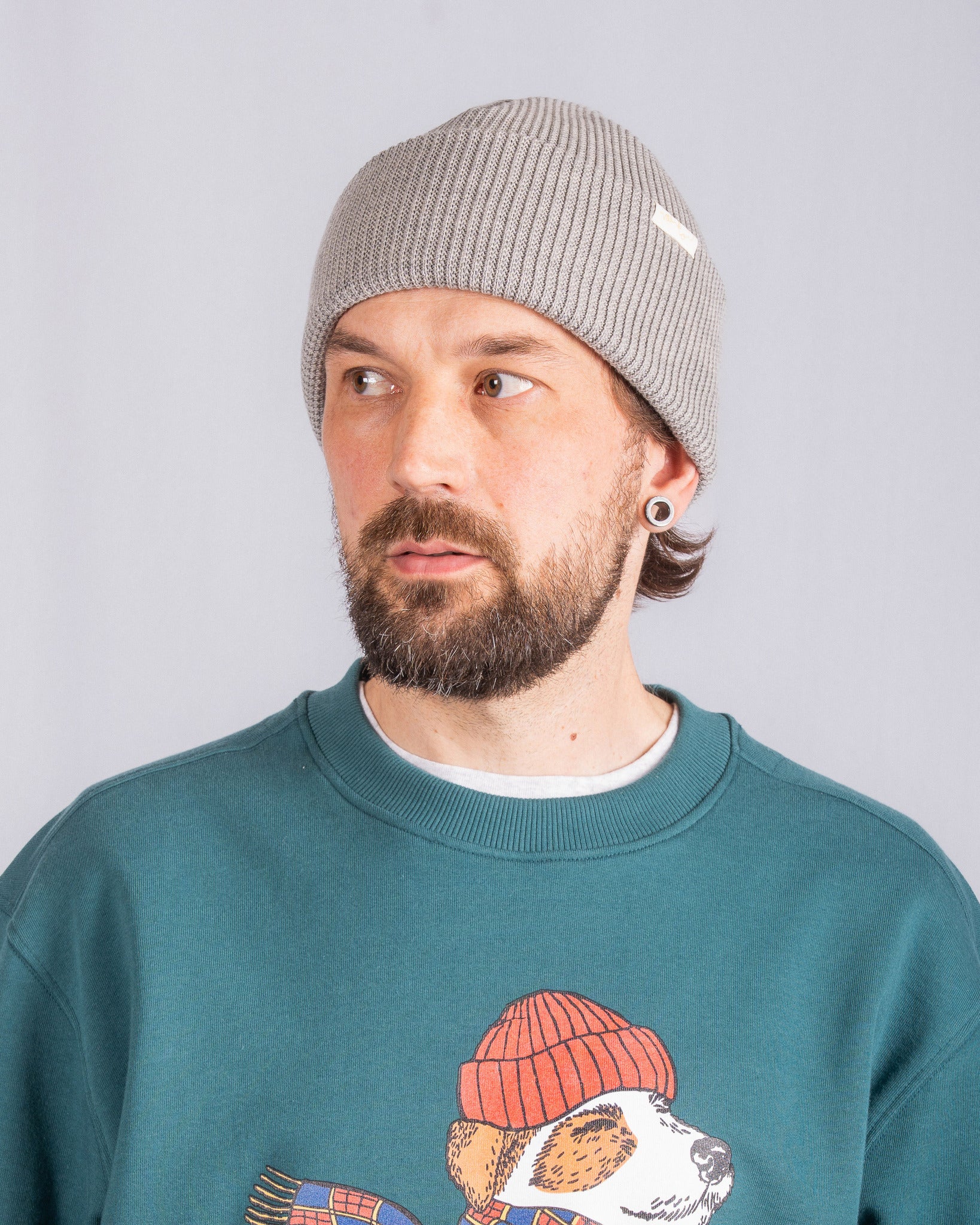 Man with a beard in a gray beanie and teal sweatshirt with a dog graphic, looking to the side.