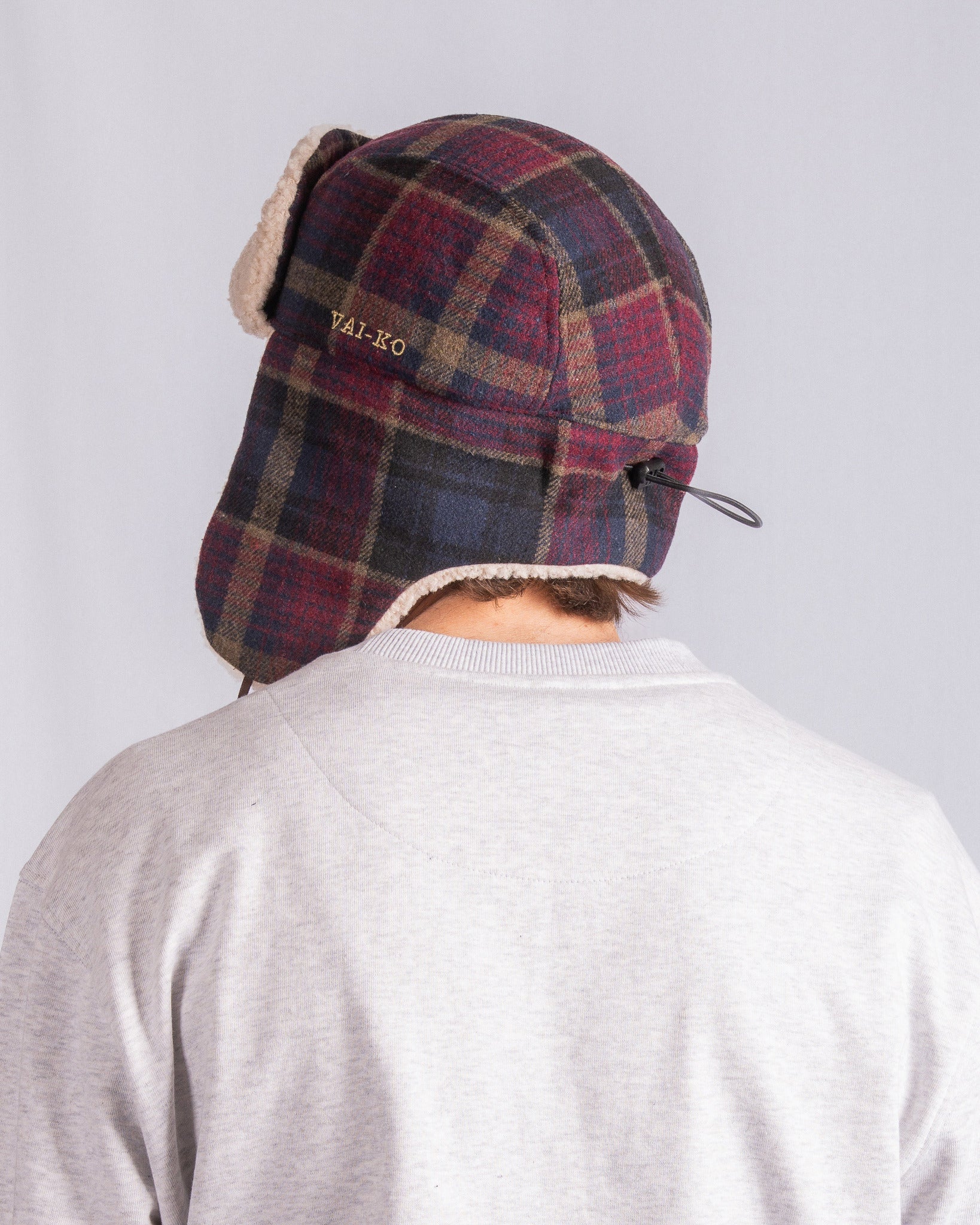 Person wearing a plaid winter hat and light gray shirt, seen from behind against a plain background.