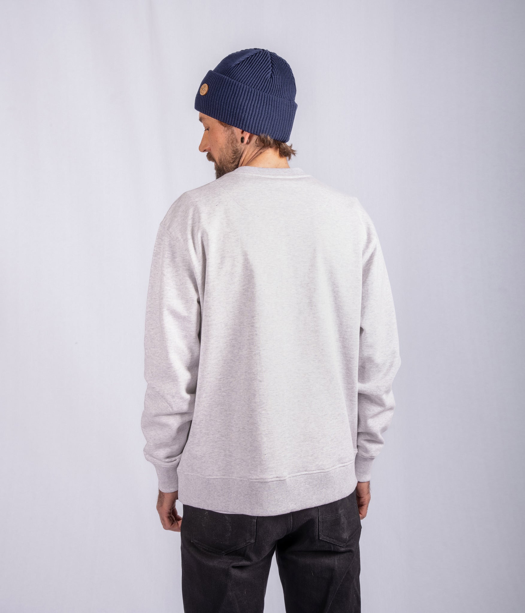 Person wearing a light gray sweatshirt, blue knit beanie, and black pants, facing away from the camera.