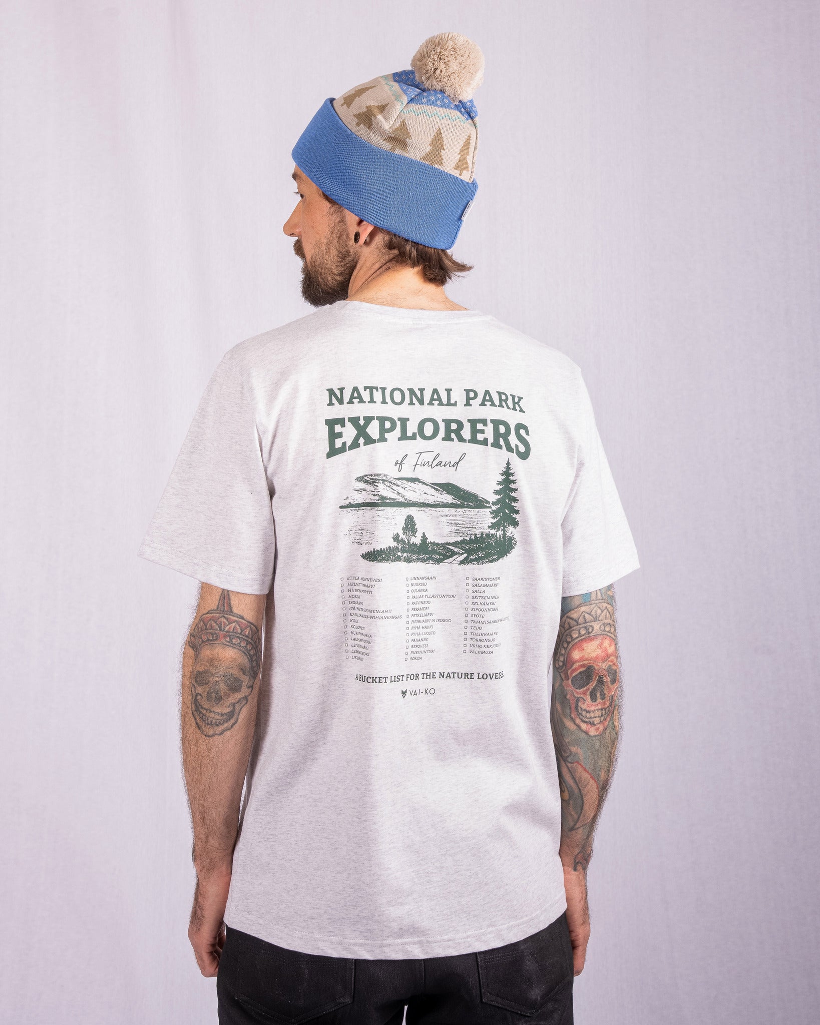 Man in gray National Park Explorers T-shirt and blue beanie, facing away, tattoos on both arms.