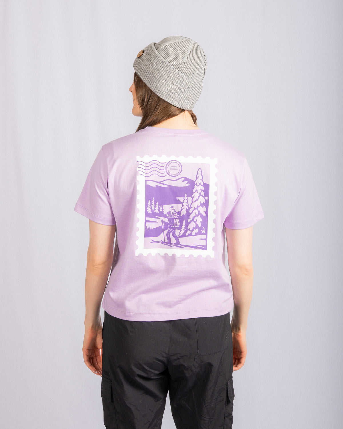 Person wearing a gray beanie and lavender shirt with a purple outdoor scene graphic, standing facing away.