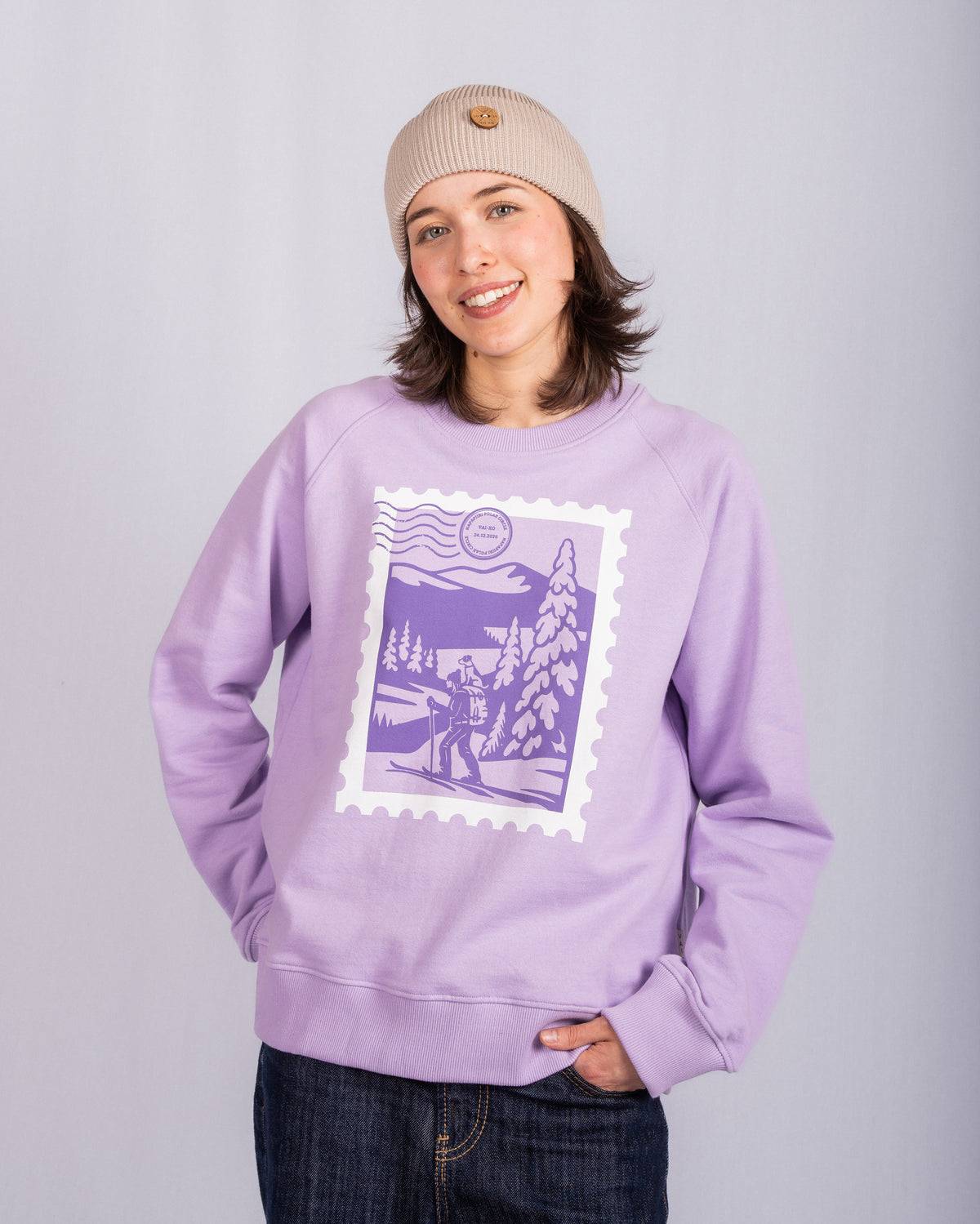 Smiling person in a beige beanie and lavender sweatshirt with a purple winter landscape graphic.