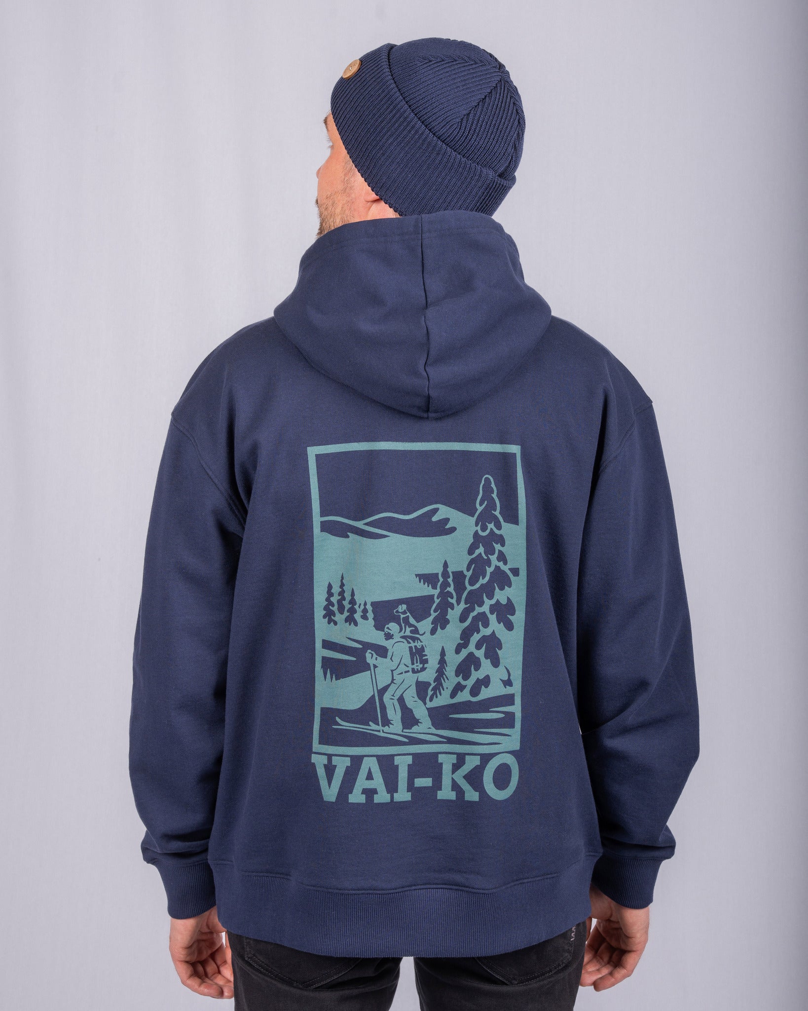 Man in a navy hoodie and beanie, with a nature scene and VAI-KO logo on the back of the hoodie.