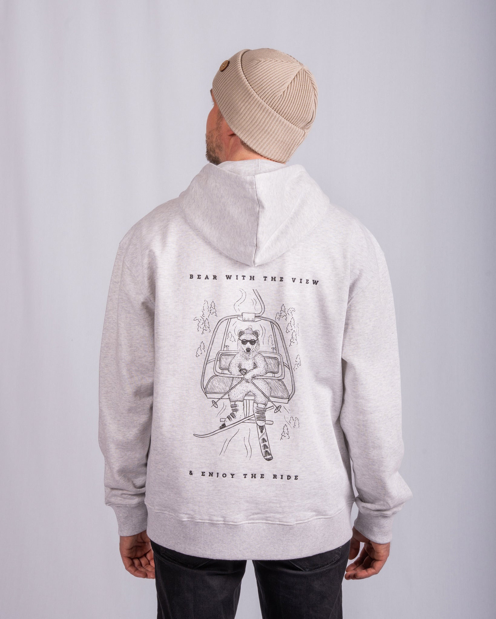 Man in beige beanie and light hoodie with astronaut bear graphic and text Bear with the view & enjoy the ride..