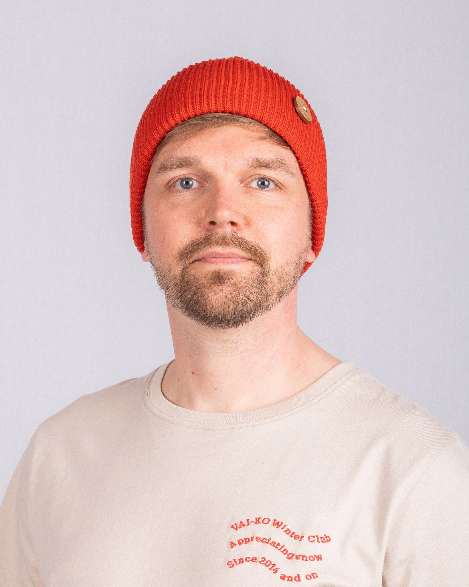 Man with a short beard wearing a red beanie and beige shirt, facing forward against a plain background.