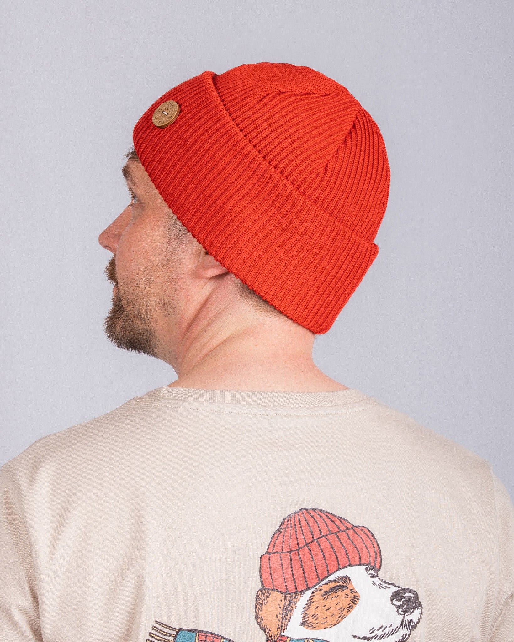 Man in a red beanie and beige shirt with a dog wearing a red beanie illustration on the back.