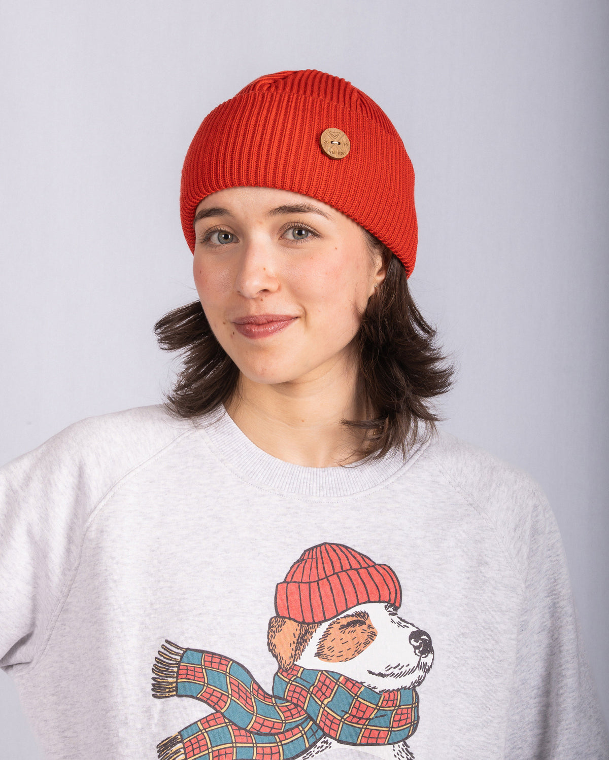 Woman in a red beanie and gray sweater with a dog wearing a hat and scarf illustration, smiling gently.