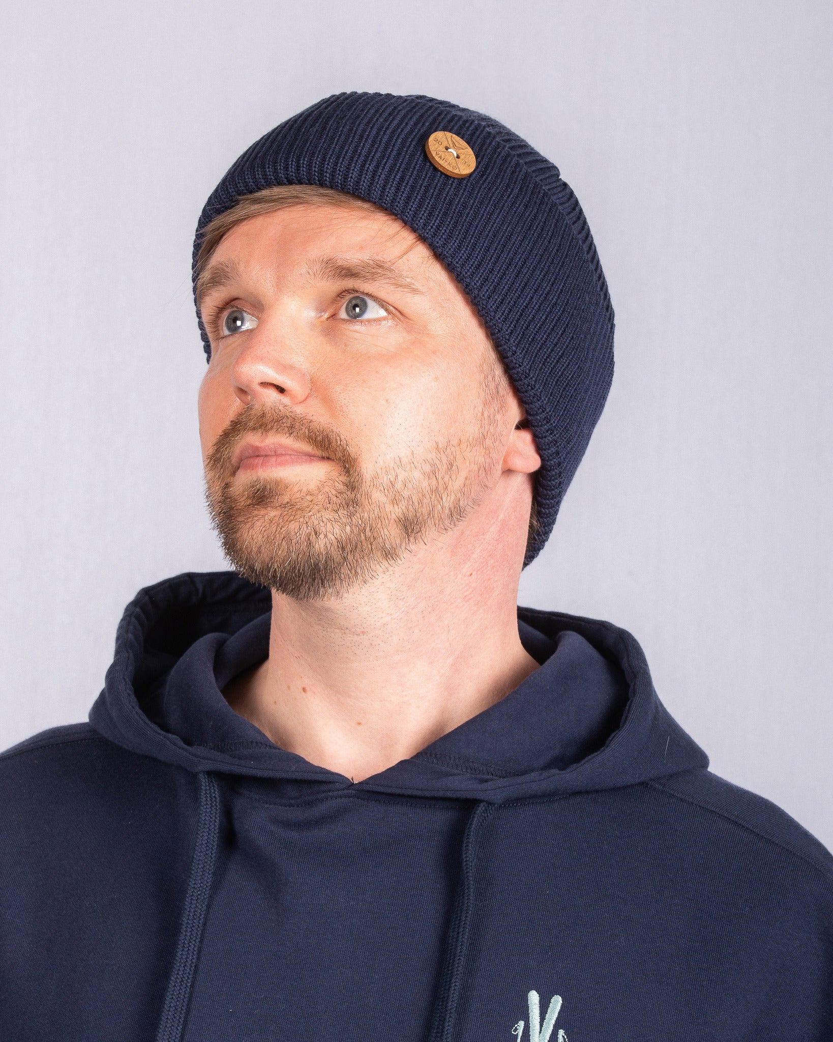 Man with a short beard wearing a navy beanie and navy hoodie, looking up and to the left.