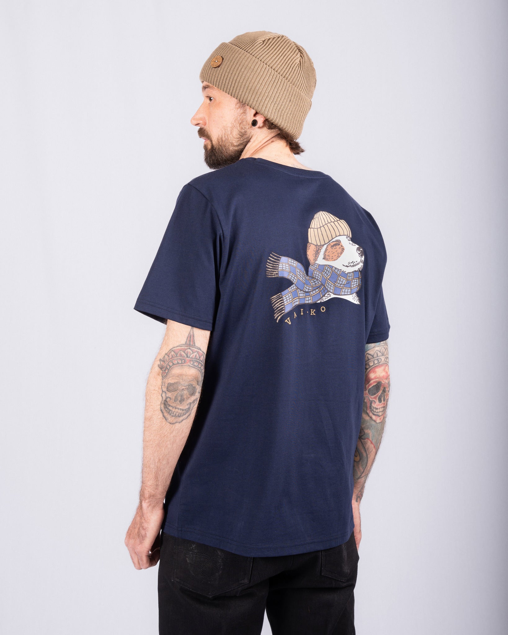Man in navy shirt and tan beanie, showing shirts back design of a dog wearing a hat and scarf.